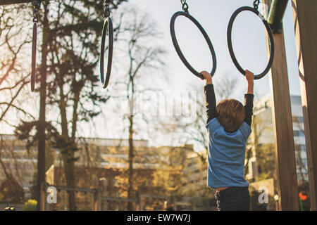 Boy hanging from rings at playground, USA Stock Photo