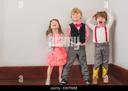 Three children dressed up in smart clothing messing about Stock Photo