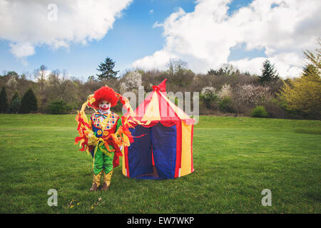 Boy dressed as a clown standing in front of a toy circus tent Stock Photo