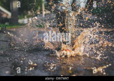 Close-up of child's legs splashing in a puddle of water