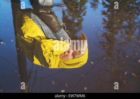 Reflection of boy in rain coat looking into puddle of water Stock Photo