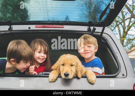 Three children sitting in the trunk of a car with their new puppy, USA