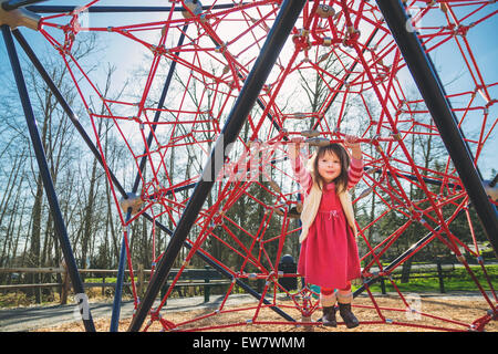 Girl playing on a red climbing frame in a park, USA Stock Photo