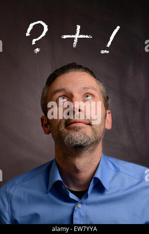Business man in front of a chalkboard looking up to a question and an exclamation mark Stock Photo
