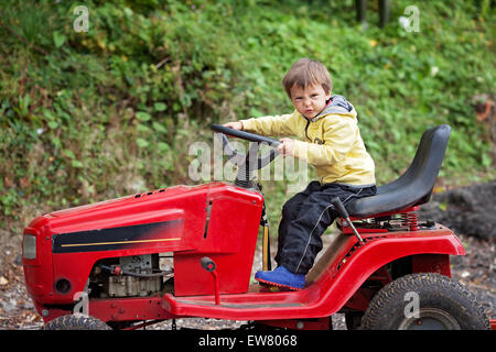 Adorable little boy, pretending to ride a lawn mower, making funny faces Stock Photo