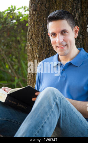 Young hispanic man reading book in park in Florida Stock Photo