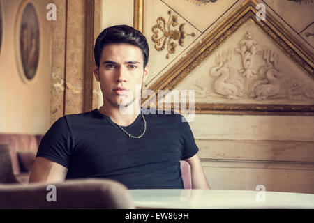 Handsome young man sitting in vintage retro elegant place in Europe, looking at camera Stock Photo