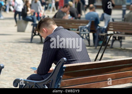 Man in suit checking mobile phone sat on bench in Old Market Square Hitchin Hertfordshire England Stock Photo