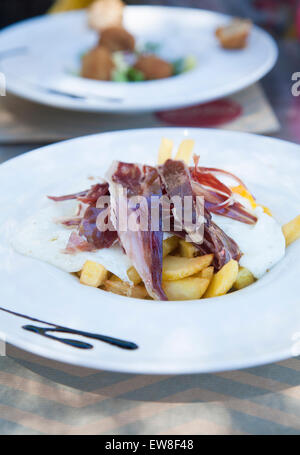 still life of white dish with typical Spain food named huevos rotos or broken eggs with potatoes french fries fried eggs and sli Stock Photo