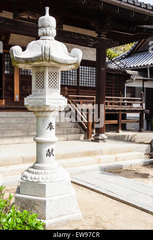 Japan, Onomichi, Jikoji Buddhist temple. New looking stone pedestal lantern, toro, with inscription on, standing outside main hall in bright sunshine. Stock Photo