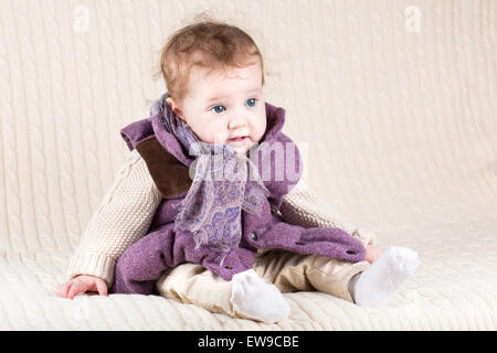 Funny baby girl in a warm purple jacket on a knitted blanket Stock Photo