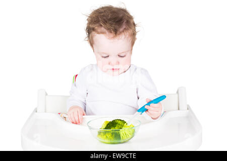 Cute baby with big blue eyes having broccoli for lunch Stock Photo