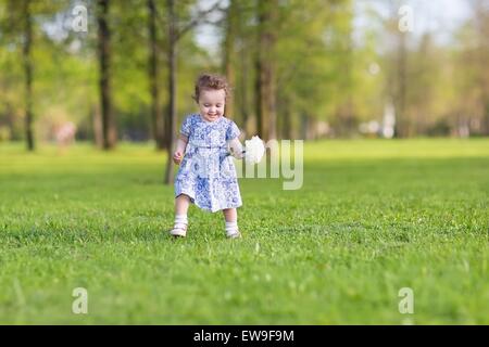 Beautiful baby girl in a blue dress running with a big white aster flower Stock Photo