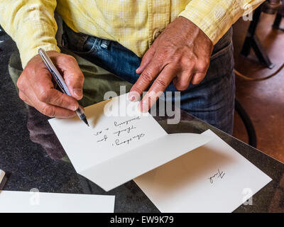 A man with weathered hands writes a thank you note in beautiful cursive writing to a customer who purchased one of his goods. Stock Photo