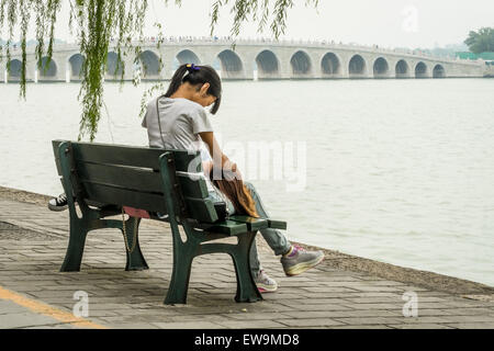 Two girls on a bench with the amazing 17 Arch Bridge in the background at Kunming Lake, Beijing, China Stock Photo