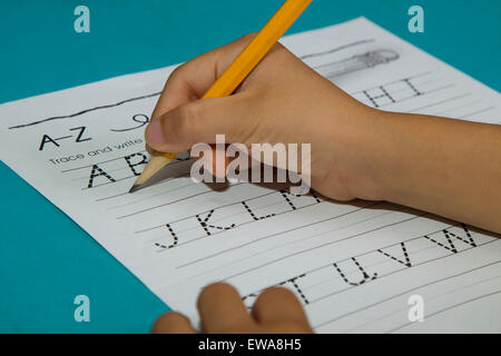 Asian boy's hand starts writing alphabet A with a yellow pencil on a blue table Stock Photo