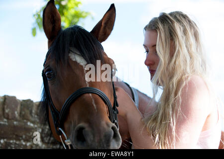 A young woman putting a bridle on a horse Stock Photo