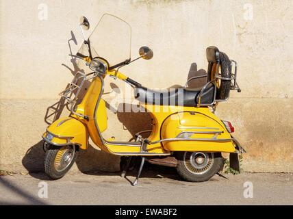 yellow retro motorcycle standing against wall Stock Photo