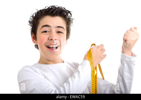 Smiling Caucasian boy with soft and smooth skin in white long sleeved t-shirt measuring the muscle of his left arm with a yellow tape measure Stock Photo