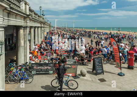 Brighton, UK. 21st June, 2015. Busy seafront. People relax on a restaurant terrace. Onlookers stand at the barriers. Credit:  Slawek Staszczuk/Alamy Live News Stock Photo