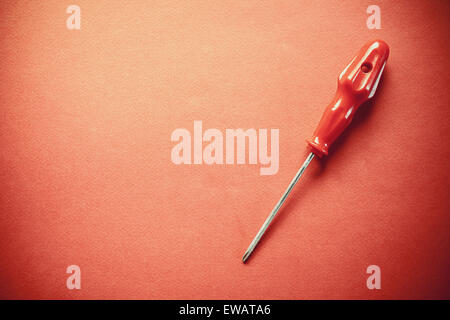 Just one red used screwdriver, simple composition on red background, left side empty. Stock Photo