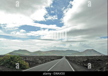 Lanzarote, Canary Islands, Spain. A straight long asphalt road in the middle of a volcanic plain, proceeding far in the horizon.