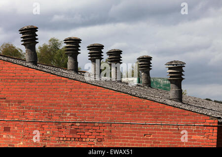 Old factory with asbestos chimney pots/flues  visible above the roof line, asbestos roof and red brick wall very expensive works Stock Photo