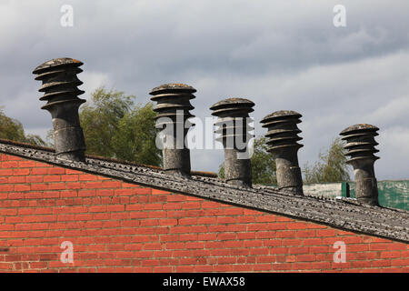 Old factory with asbestos chimney pots/flues  visible above the roof line, asbestos roof and red brick wall very expensive works Stock Photo