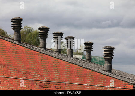 Old factory with asbestos chimney pots/flues  visible above the roof line, asbestos roof and red brick wall very expensive works Stock Photo