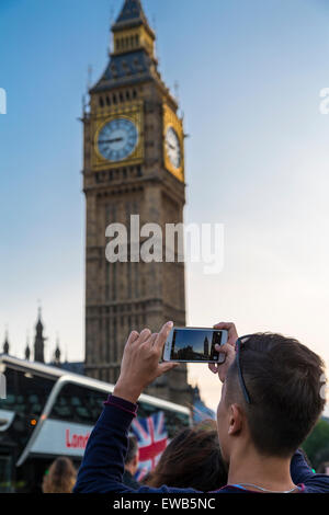 Portrait image of a tourist taking a picture of Big Ben on a smart phone from Westiminster Bridge on a clear summer's evening, London, England, UK Stock Photo