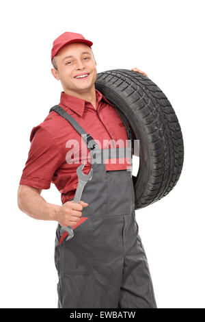 Vertical shot of a young cheerful mechanic holding a tire in one hand and a wrench in the other isolated on white background Stock Photo