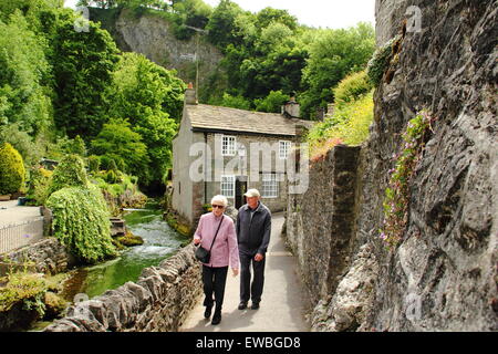 A elderly man & woman pass by stone built cottages on Peakshole Water in  Castleton village, Peak District Derbyshire UK Stock Photo