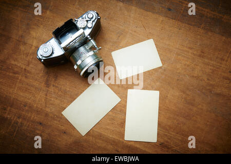 Vintage old retro film camera and old empty paper frame photos on wooden background. Nostalgic style picture, memories, Stock Photo