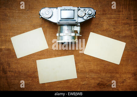 Vintage old retro film camera and old empty paper frame photos on wooden background. Nostalgic style picture, memories, Stock Photo