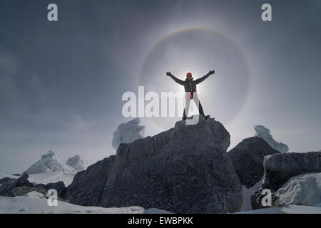 A man stands infront of the sun as it produces a large halo from ice crystals in the sky. Stock Photo