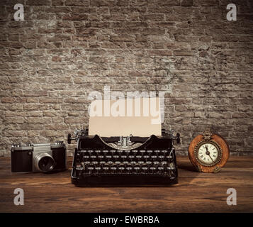 Retro typewriter, alarm-clock and camera placed on wooden planks. Old brick wall as background with copyspace. Stock Photo