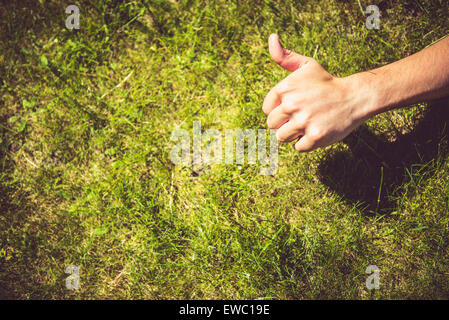 Thumbs up sign against the green grass on a sunny day Stock Photo