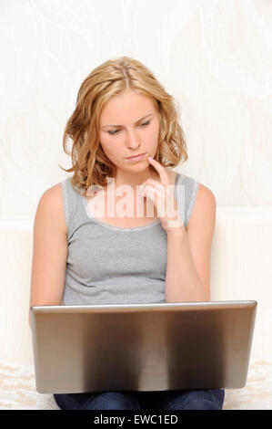 Thoughtful young woman sitting with laptop Stock Photo