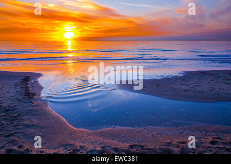 Orange sunset at coast with sea and beach Stock Photo