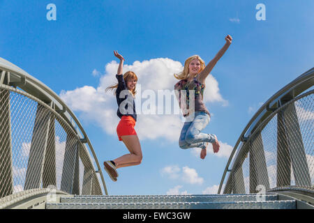 Two happy and enthusiastic teenage girls jumping on bridge in front of blue sky Stock Photo
