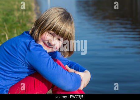 Young european girl sitting at waterfront of river Stock Photo