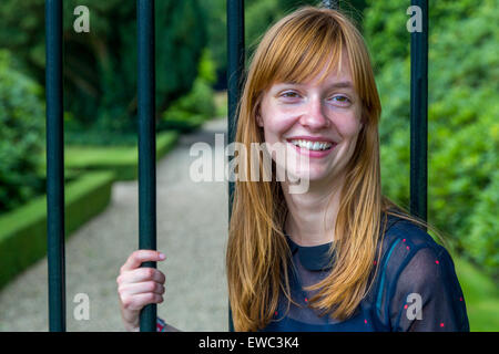 Red haired dutch teenage girl laughing holding metal bar of gate Stock Photo