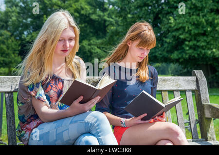 Two caucasian teenage girls reading books on bench in green nature Stock Photo