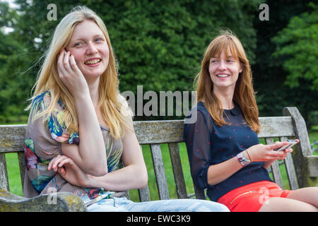 Two european teenage girlfriends sitting on bench in park with mobile phone Stock Photo