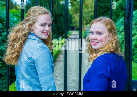 Two caucasian teenage sisters looking back at fence of garden Stock Photo