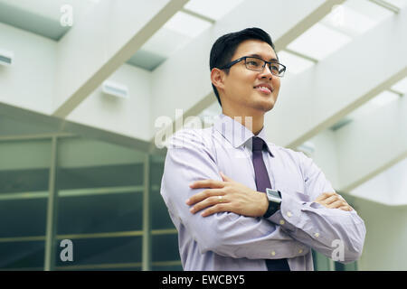 Portrait of happy and confident young asian businessman. The man stands in a street against office buildings and crosses arms lo Stock Photo