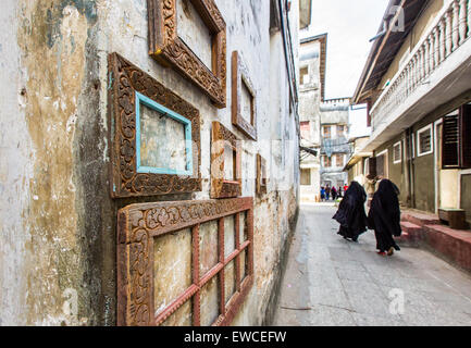 Veiled women walk past picture frames in Stone Town, Zanzibar. Stock Photo