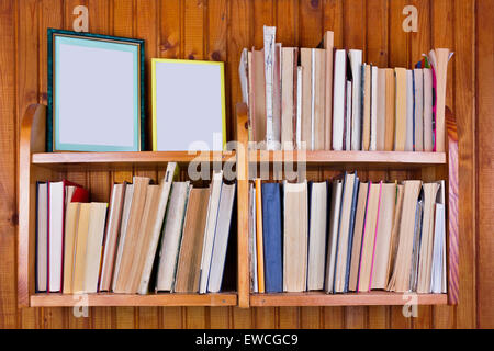 The old forgotten decrepit books and photos on the wooden shelf. The wall of the rural house is upholstered with pine laths. The Stock Photo