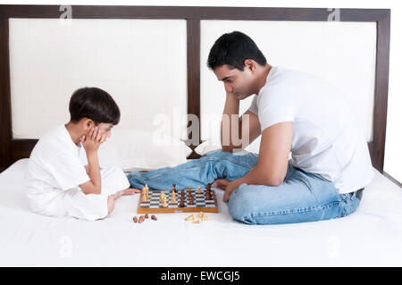 Father and son sitting on bed and playing chess Stock Photo