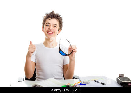 Acne Caucasian teenager makes success gesture with right thumb up holding black plastic 3D Cinema eyeglasses while doing homework Stock Photo